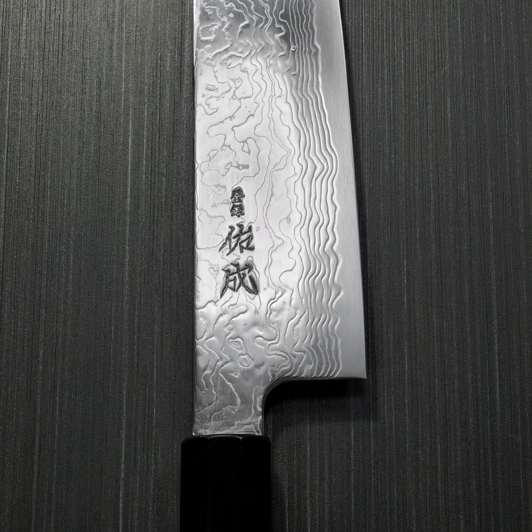 Macro detail of a Damascus steel blade stamped with a Japanese maker's signature